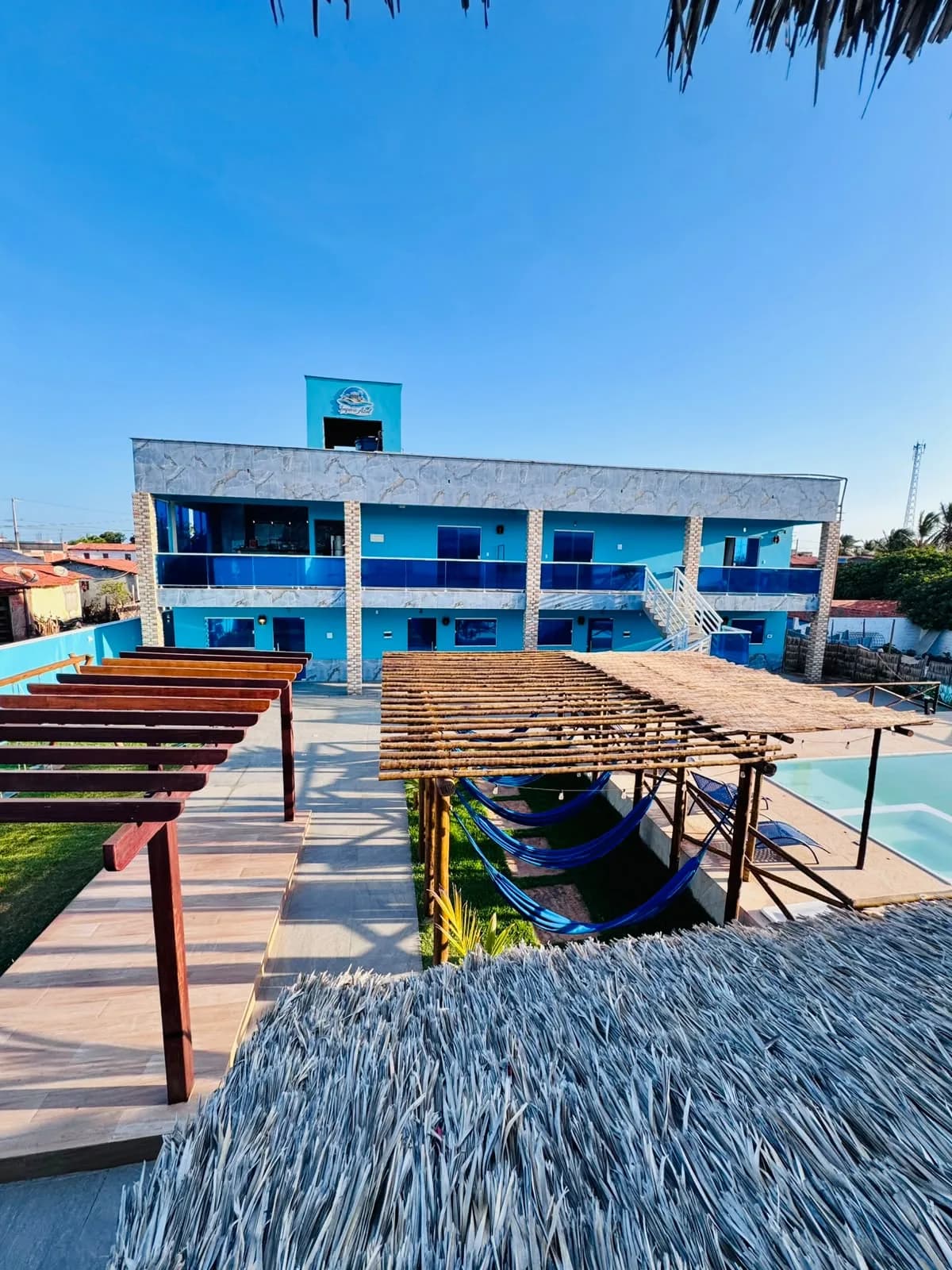 Fachada da Pousada Império Azul: prédio azul de dois andares com varandas de vidro, redário e piscina à frente