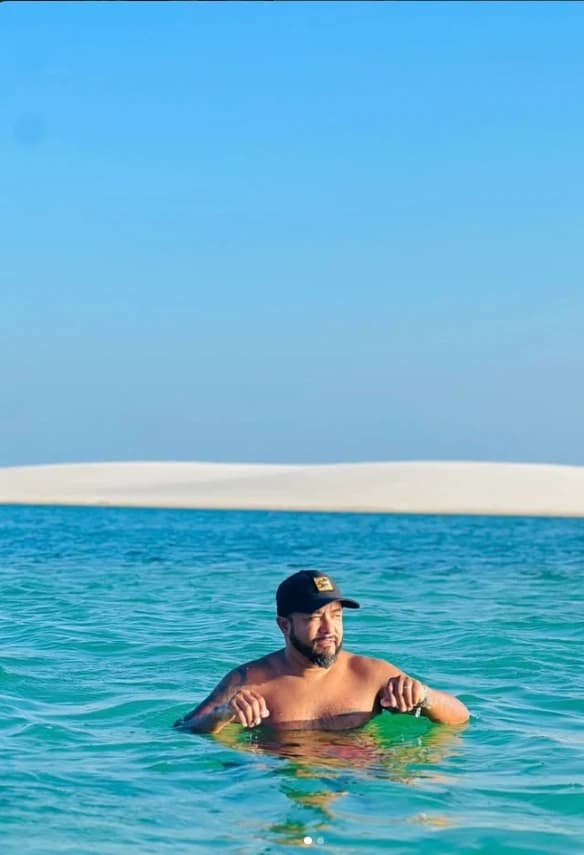 Visitante se banhando em lagoa de água verde-azulada com dunas ao fundo