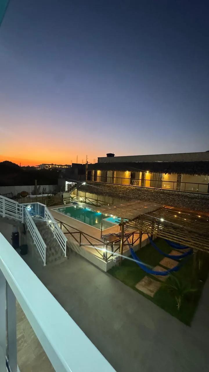 Vista do alto da pousada ao entardecer, com a piscina iluminada, o redário e o céu alaranjado